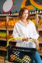 Vertical portrait of beautiful young woman customer holding basket of fruits standing at fruit and vegetables section of Royalty Free Stock Photo