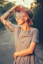 Vertical portrait of blonde girl with short haircut posing to in forest on sunset background. She wears hat, sunglasses Royalty Free Stock Photo