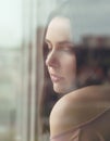 Vertical portrait of Brunette girl standing behind window with city reflection on glass Royalty Free Stock Photo