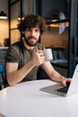 Vertical portrait of cheerful bearded young businessman holding in hand cup with morning coffee sitting at table with Royalty Free Stock Photo