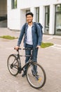 Vertical portrait of cheerful handsome young delivery man in protective helmet posing standing near bicycle in city Royalty Free Stock Photo