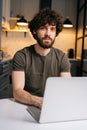 Vertical portrait of confident bearded young business man using on laptop sitting at table in kitchen room with modern Royalty Free Stock Photo