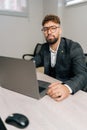 Vertical portrait of confident businessman wearing stylish suit and eyeglasses working on laptop at office desk Royalty Free Stock Photo