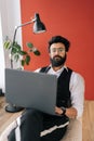 Vertical portrait of confident Indian business man in elegant formalwear working on laptop sitting on chair in light Royalty Free Stock Photo