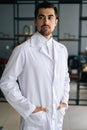 Vertical portrait of confident male doctor wearing white medical uniform standing in hospital office, looking away. Royalty Free Stock Photo