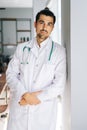 Vertical portrait of confident male doctor wearing white medical uniform standing with stethoscope in hospital office Royalty Free Stock Photo