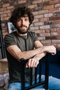 Vertical portrait of confident smiling young man looking at camera sitting on chair and holding to chairbac in cozy Royalty Free Stock Photo