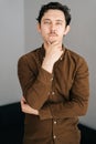 Vertical portrait of confident young man with little moustache holding hand on chin and thoughtful looking at camera Royalty Free Stock Photo