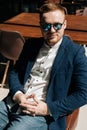 Vertical portrait of confident young man in sunglasses wearing stylish suit wear sitting in armchair, looking in camera. Royalty Free Stock Photo