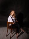 Vertical portrait of a cute barefoot blonde sitting on a chair in the studio