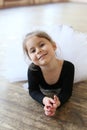 Vertical portrait of a cute smiling little ballerina lying on the floor in a ballet class Royalty Free Stock Photo