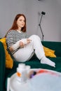 Vertical portrait of depressed young woman with broken right hand wrapped in white gypsum bandage sitting on couch