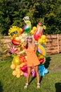 Vertical portrait of elegant blonde female in summer dress and sunglasses holding drinking glass, posing with colorful Royalty Free Stock Photo