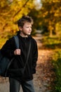Vertical portrait of European fair-haired a teenager in black jacket with backpack on background of orange trees Royalty Free Stock Photo