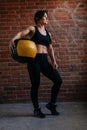 Vertical portrait of fitness young athletic woman with strong body in black sportswear posing with heavy medicine ball Royalty Free Stock Photo