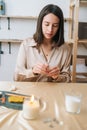 Vertical portrait of focused young woman putting thread through eye of needle at table in modern workshop. Royalty Free Stock Photo