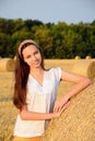 Vertical portrait of a girl in a white blouse, standing against a background of bales of straw and smiling, close up