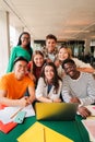 Vertical portrait. Group of young teenage students siting at library, using a laptop and looking at camera. Happy Royalty Free Stock Photo