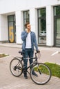 Vertical portrait of handsome young man in casual clothing standing with bicycle in city street and talking on mobile Royalty Free Stock Photo