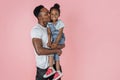 Vertical portrait of happy afro daddy embracing with his cute baby daughter, pink studio background. Royalty Free Stock Photo