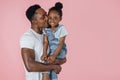 Vertical portrait of happy afro daddy embracing with his cute baby daughter, pink studio background. Royalty Free Stock Photo