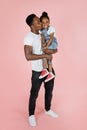 Vertical portrait of happy afro daddy embracing with his cute baby daughter, pink studio background. Royalty Free Stock Photo