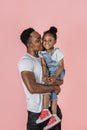 Vertical portrait of happy afro daddy embracing with his cute baby daughter, pink studio background. Royalty Free Stock Photo