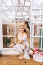 Vertical portrait of happy blonde young woman in beautiful dress sitting in doorstep of summer gazebo house on sunny day Royalty Free Stock Photo