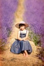 Vertical portrait of happy cute little girl wearing blue dress and white hat and sitting in lavender field with violet flowers Royalty Free Stock Photo