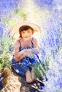 Vertical portrait of happy cute little girl wearing blue dress and white hat and sitting in lavender field with violet flowers Royalty Free Stock Photo