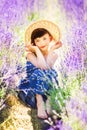 Vertical portrait of happy cute little girl wearing blue dress and white hat and sitting in lavender field with violet flowers Royalty Free Stock Photo