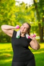 Vertical portrait of a happy plus-size model with dumbbells during a workout in a summer