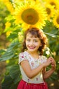 Vertical portrait of happy smiling 4 years old curly girl in sunflowers field with big bright yellow sunflower in sunny summer day Royalty Free Stock Photo