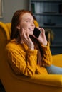 Vertical portrait of happy smiling young woman talking on smartphone sitting in yellow chair at home. Pretty lady having Royalty Free Stock Photo