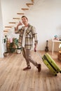 Vertical portrait of happy young man going on holiday, shows mobile phone call hand gesture, walking with suitcase Royalty Free Stock Photo