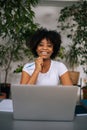 Vertical portrait of laughing curly black young woman holding pen in hand, smiling looking at camera sitting at table in Royalty Free Stock Photo