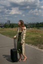 Vertical portrait of a lonely young woman with a suitcase against the backdrop of urban landscapes