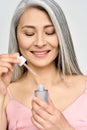 Vertical portrait of mature Asian woman holding pipette and bottle serum.