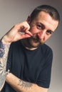 Vertical portrait of a middle-aged tattooed man touching his brown mustache and looking at camera over gray background.