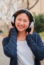 Vertical portrait of one chinese young woman listening music with headphones using wireless connection. Happy asian girl Royalty Free Stock Photo