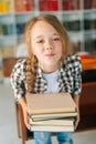 Vertical portrait of playful elementary child school girl holding stack of books in library at school, looking at camera Royalty Free Stock Photo