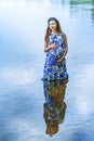 Vertical portrait of pregnant woman expecting baby standing in water in blue dress with hands on her belly. Summer portrait of