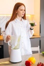 Vertical portrait of pretty redhead young woman holding glass with green vegetable detox smoothie cocktail from blender Royalty Free Stock Photo