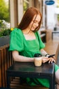 Vertical portrait of pretty smiling young woman using browsing smartphone looking at screen, sitting at table with Royalty Free Stock Photo