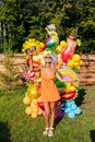 Vertical portrait of pretty tanned blonde female in summer dress and sunglasses posing with various colorful festive