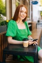 Vertical portrait of pretty young woman holding mobile phone sitting at table with coffee cup in outdoor cafe terrace in Royalty Free Stock Photo