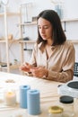 Vertical portrait of pretty young woman putting thread through eye of needle at table in modern workshop. Royalty Free Stock Photo