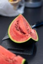 Vertical portrait of a quarter piece of a green cut watermelon lying on a plastic cutting board next to a knife. The slice of the