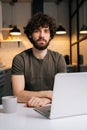 Vertical portrait of confident bearded young business man using on laptop sitting at table in kitchen room with modern Royalty Free Stock Photo