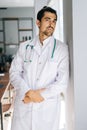 Vertical portrait of serious male doctor wearing white medical uniform standing with stethoscope in hospital office Royalty Free Stock Photo